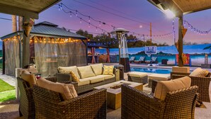 Un patio al aire libre con mobiliario de mimbre, una zona de estar cubierta y una piscina.