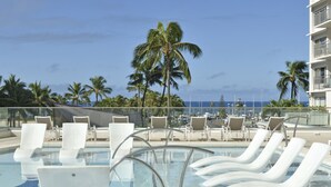 A pool area with white lounge chairs and a clear view of the ocean and palm trees. - Inside the Ilikai Hotel & Luxury Suites, your vacay is whatever you want it!!!!e (Honolulu)