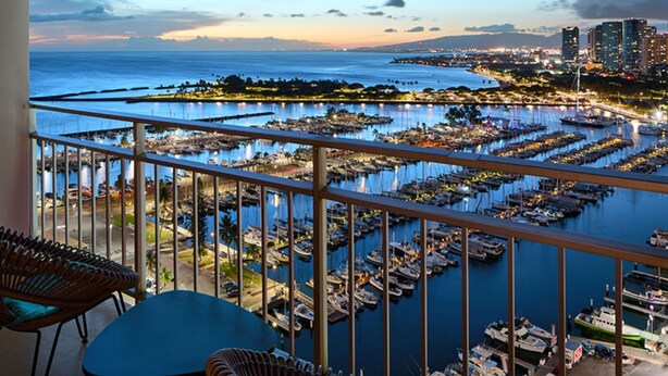 A balcony with wicker furniture overlooking a marina with numerous boats and a cityscape in the background. - Inside the Ilikai Hotel & Luxury Suites, your vacay is whatever you want it!!!!e (Honolulu)