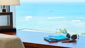 A desk with a lamp, a pair of sunglasses, a notebook, and a pen. The desk overlooks a view of the ocean and a boat. - Inside the Ilikai Hotel & Luxury Suites, your vacay is whatever you want it!!!!e (Honolulu)
