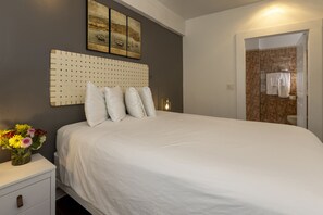 A bedroom with a large bed, a bedside table with a vase of flowers, and a headboard with a grid pattern.