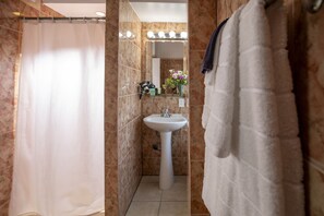 A bathroom with a shower curtain, a sink, and a mirror with lights above it.