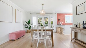 A dining area with a wooden table and white chairs, a bench, and a hanging light fixture.
