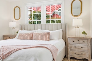 Une chambre à coucher bien aménagée, avec un grand lit, deux tables de chevet, un miroir et une fenêtre donnant sur des immeubles.