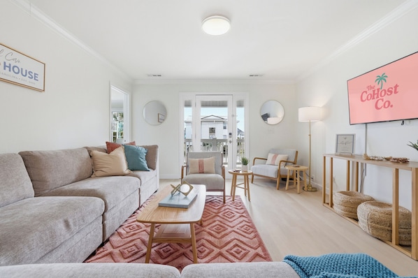 Un salon moderne avec un canapé gris, une table basse en bois et un tapis rouge à motifs. Un téléviseur est fixé au mur, et un panneau encadré est placé au-dessus.