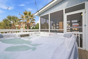 Un bain à remous sur une terrasse en bois avec une balustrade blanche, entouré de palmiers et surplombant un ciel dégagé.