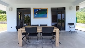 Un área de comedor al aire libre moderna, con una mesa de madera y sillas negras, un cuadro enmarcado arriba y vistas a follaje.