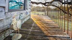 Eine Holzterrasse mit Metallgeländer, ein rustikales Gebäude mit einem Fenster und eine dekorative Hahnenfigur.