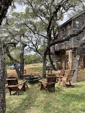 Una baita di legno rustica con un balcone, circondata da alberi alti e un'area salotto esterna.