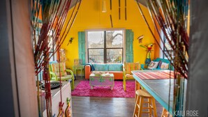 Ein gemütliches Zimmer mit einem großen Fenster, einem Sofa, einem Tisch und einem farbenfrohen Teppich.