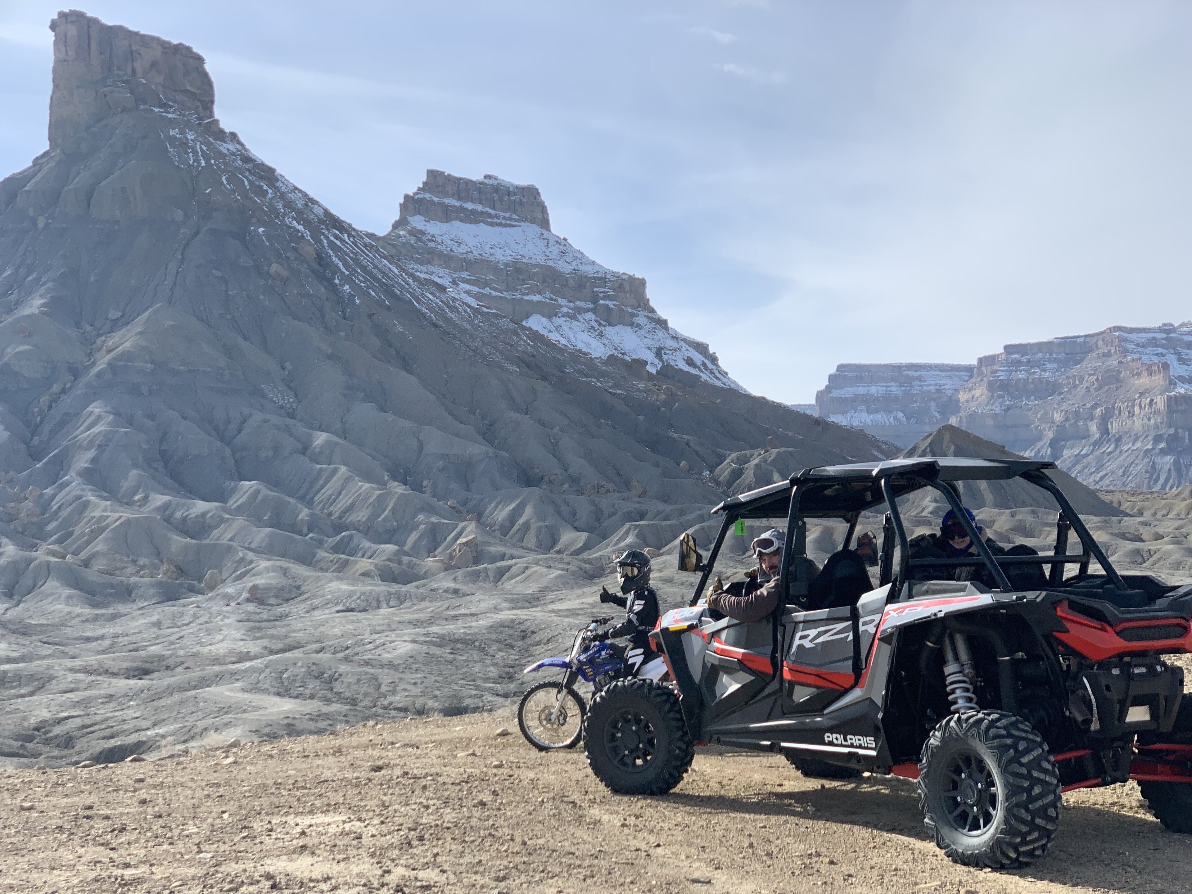 Un vehículo Polaris RZR todoterreno estacionado sobre terreno rocoso, con montañas al fondo.