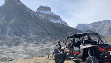 Un vehículo Polaris RZR todoterreno estacionado sobre terreno rocoso, con montañas al fondo.
