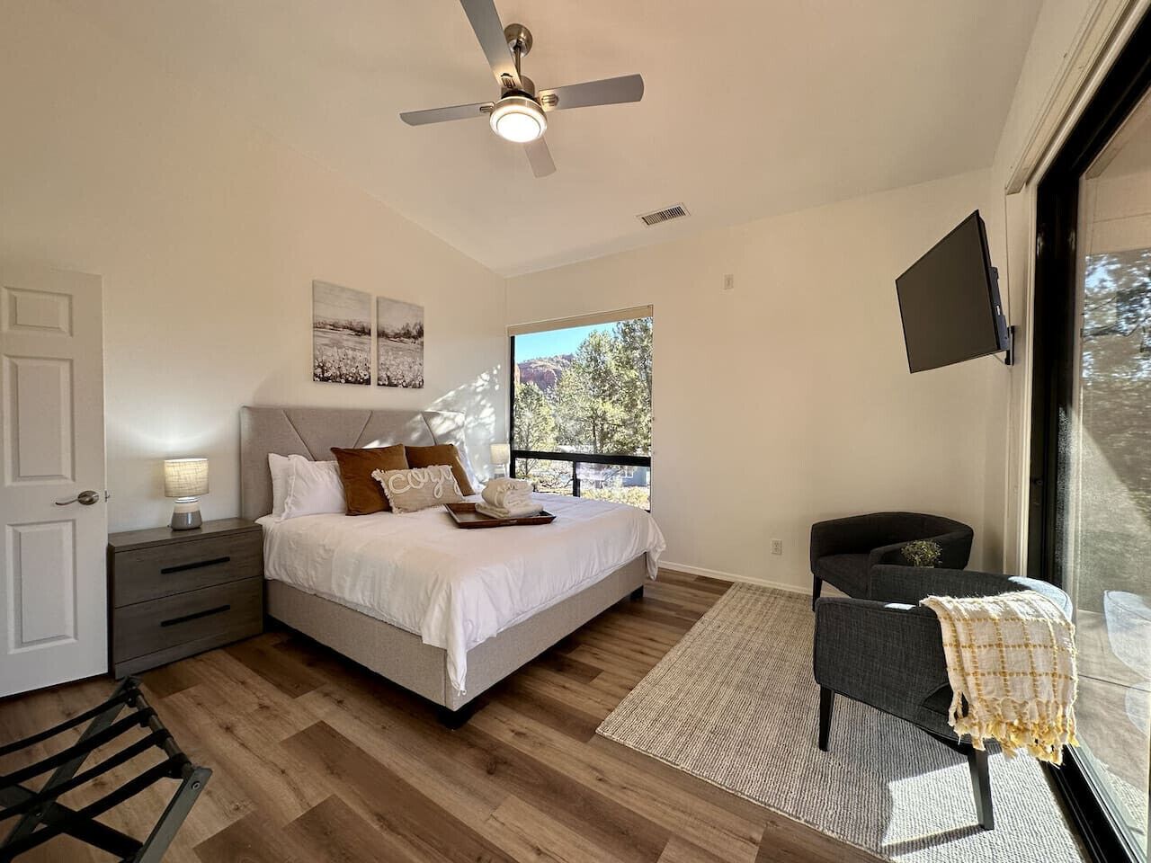 A bedroom with a bed, a nightstand, a desk, a chair, a ceiling fan, and a TV.