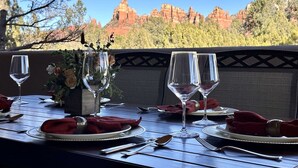 Une table dressée pour le dîner, avec des verres à vin et un vase de fleurs, offrant une vue panoramique sur des formations rocheuses rouges et des arbres.