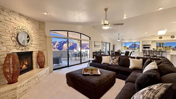 Un salon spacieux doté d’une cheminée en pierre, d’un grand canapé d’angle et offrant une vue sur les montagnes grâce à de grandes fenêtres.