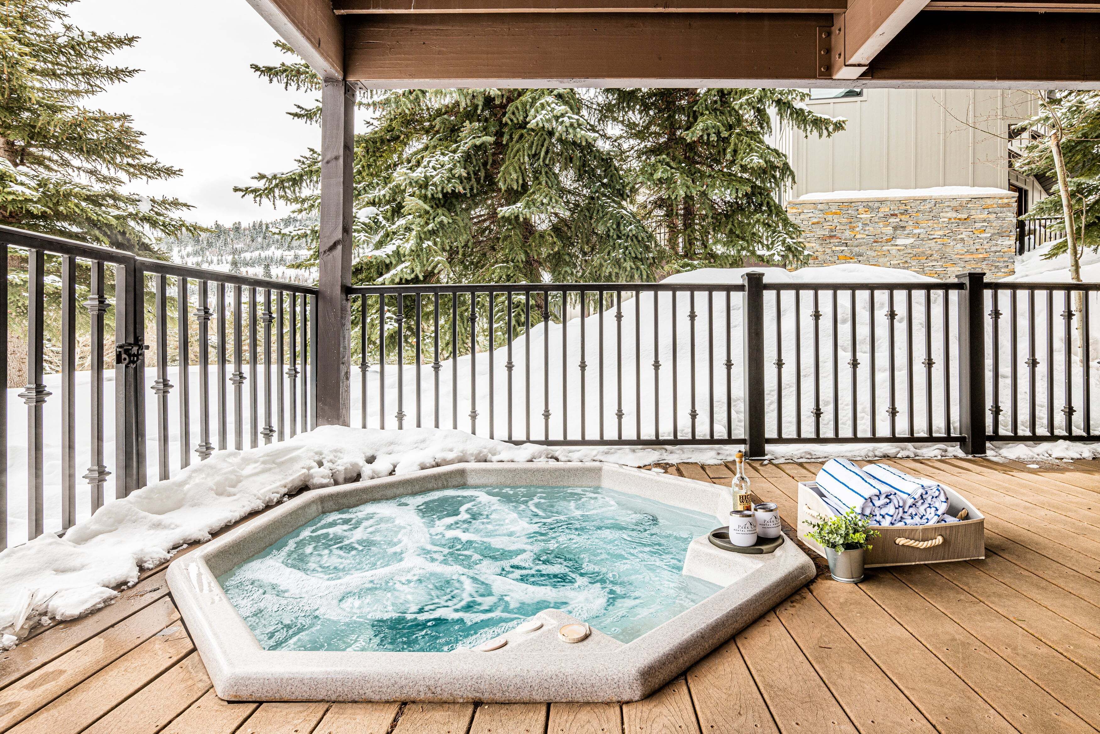 Un bain à remous sur une terrasse en bois, avec de la neige au sol et une clôture métallique en arrière-plan.