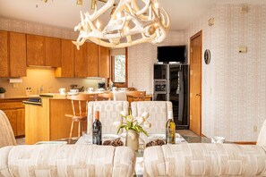 A modern kitchen with wooden cabinets, a dining area with patterned chairs, and a chandelier.