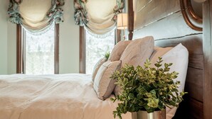 Quarto com cama, almofadas, uma planta na mesa de cabeceira e cortinas.