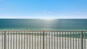 A beach view from a balcony with a railing, clear sky, and calm sea.