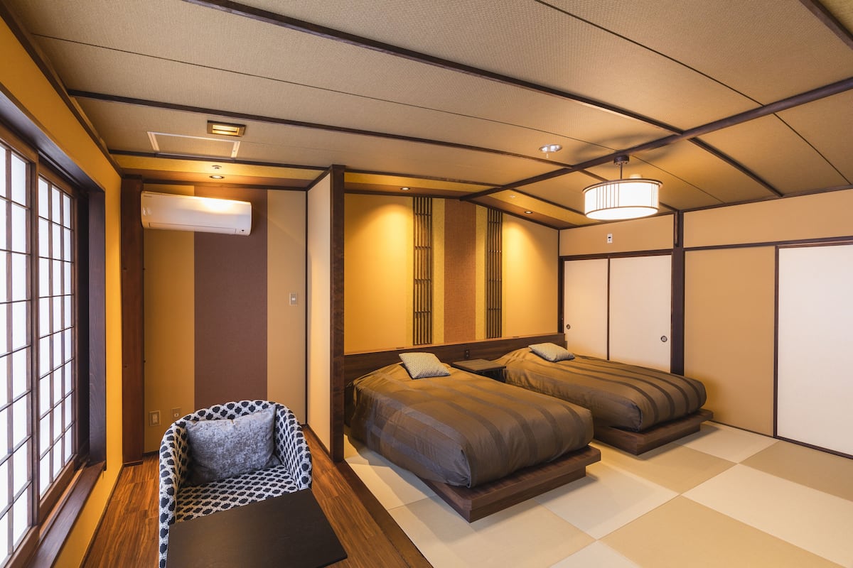 A traditional Japanese-style bedroom with tatami flooring, a futon bed, a low wooden desk, and a shoji screen door.