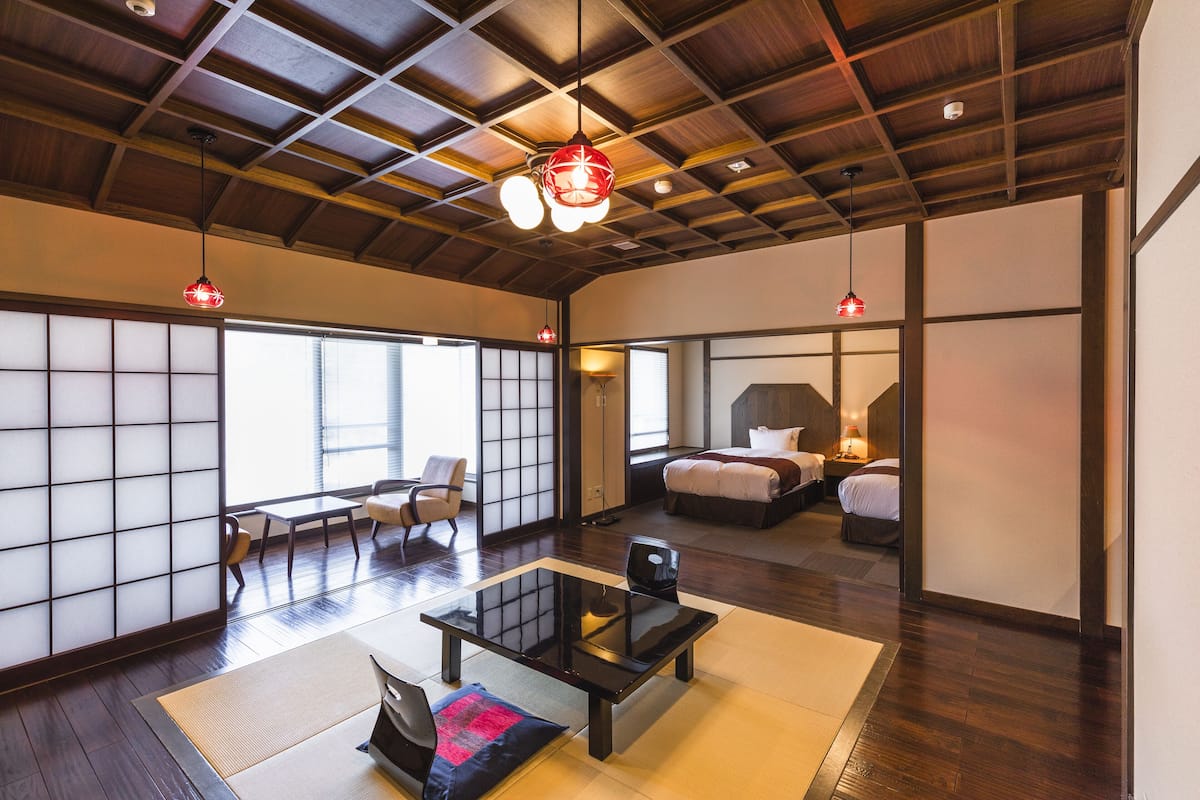 A spacious room with a traditional Japanese-style tatami mat floor, a large sliding door, and a bed with a modern design.