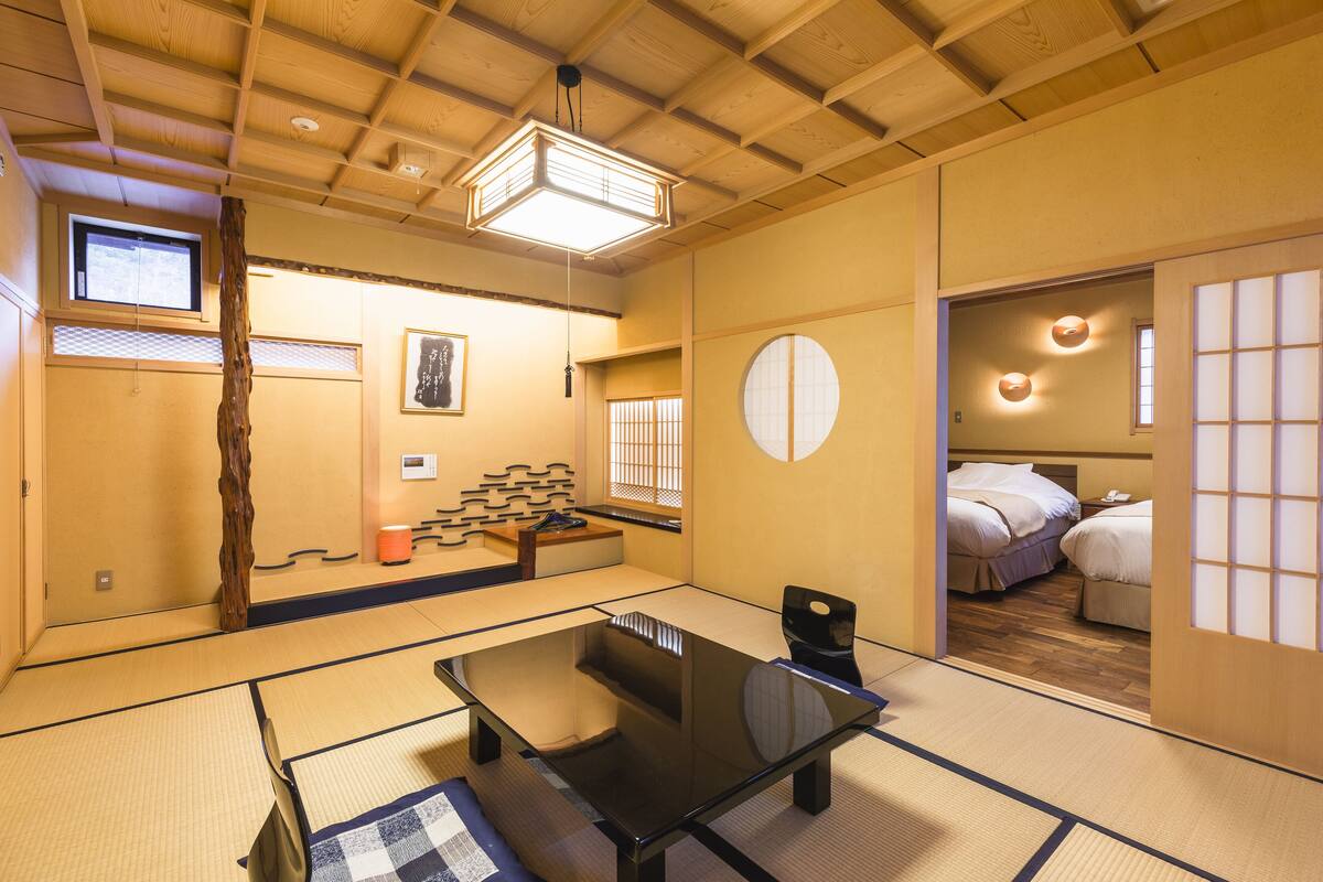 A traditional Japanese room with tatami flooring, a low table, and a bed with futon bedding.