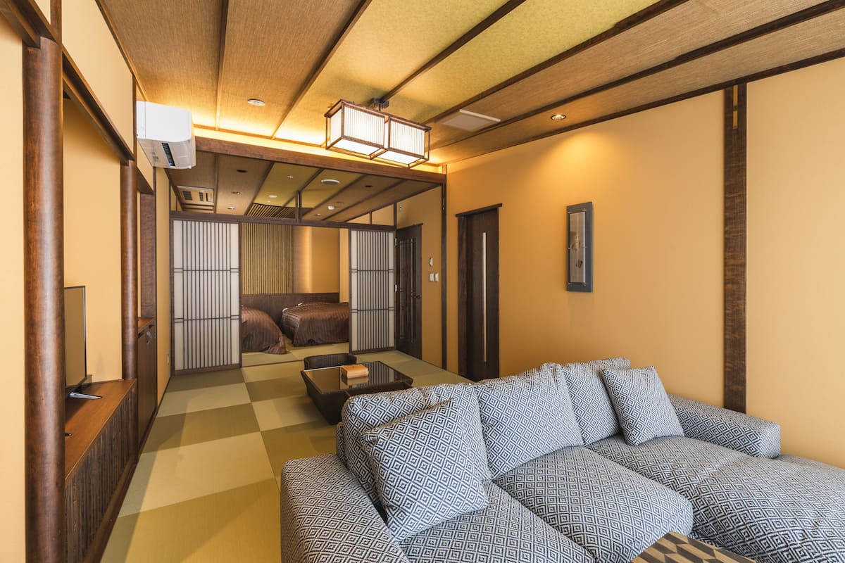 A traditional Japanese-style room with tatami flooring, a low wooden ceiling, and a sliding door leading to a separate sleeping area.