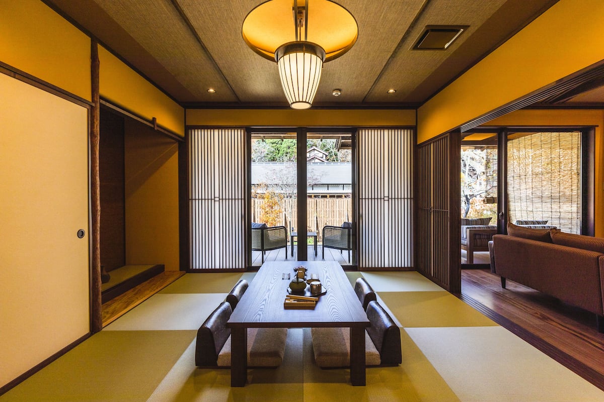 A traditional Japanese room with tatami flooring, a low table with cushions, sliding doors, and a view of the outdoors.
