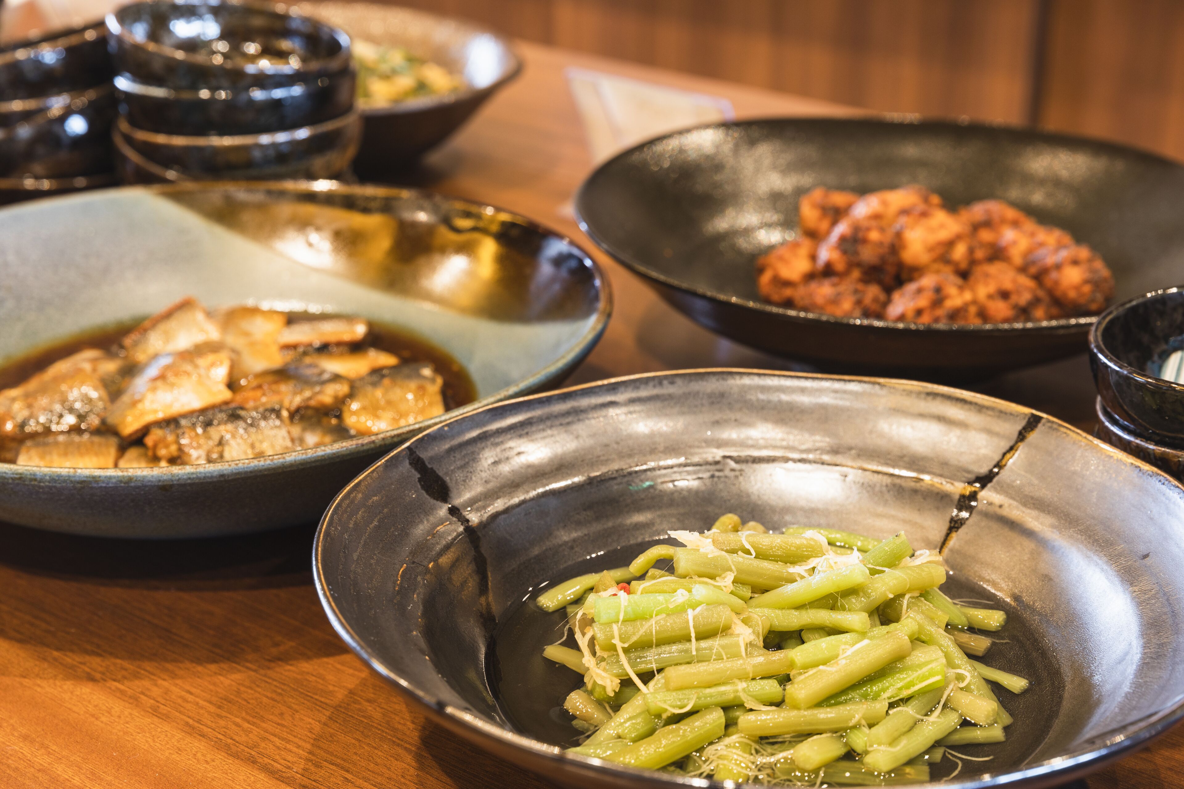 A table with various dishes including a bowl of green vegetables, a bowl of fried items, and a bowl of meat.