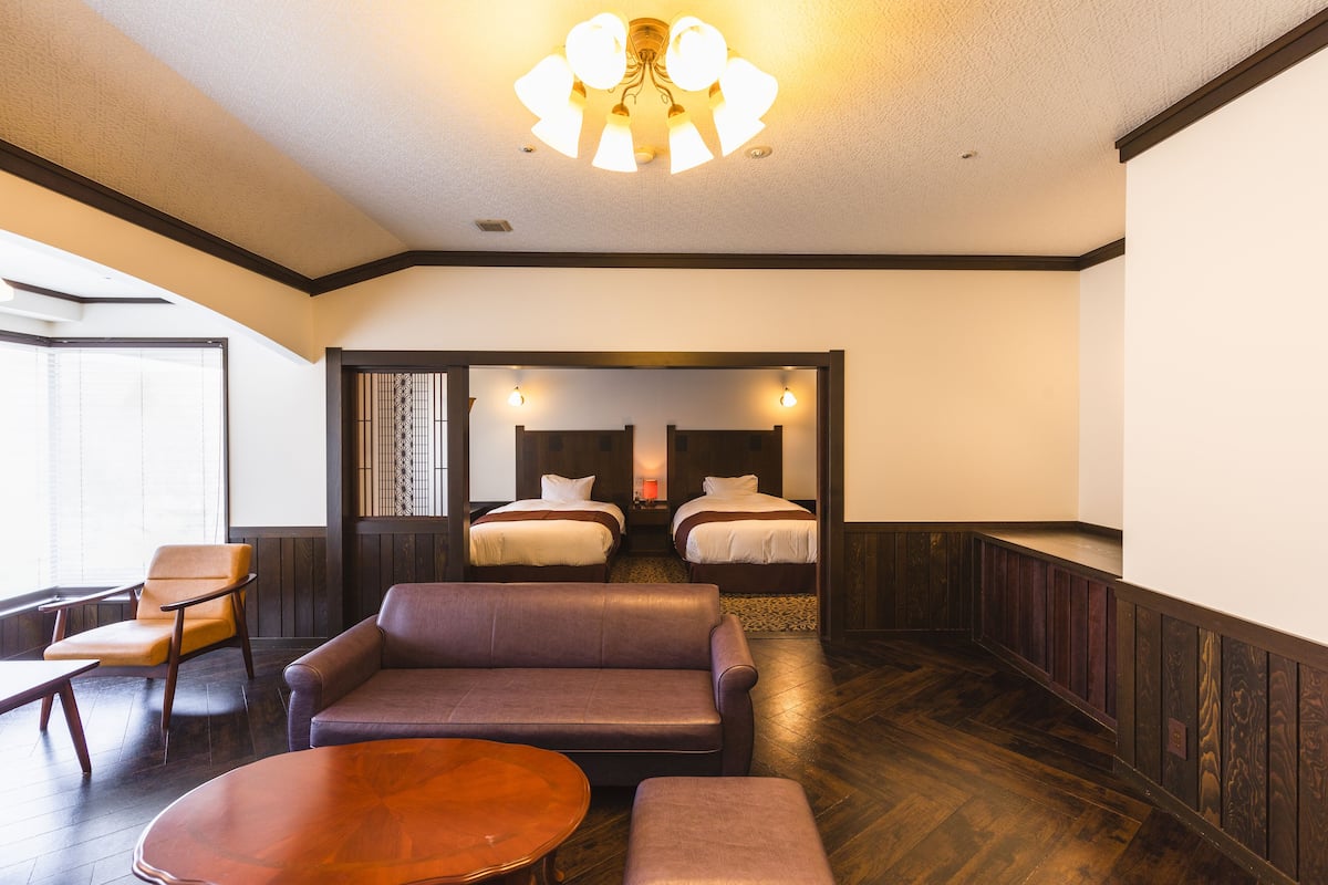A hotel room with a wooden floor, a sofa, a coffee table, and two beds with headboards.