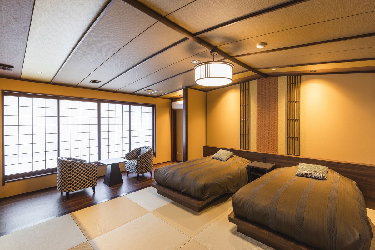 A traditional Japanese-style bedroom with tatami flooring, two beds, a shoji screen, and a hanging light fixture.