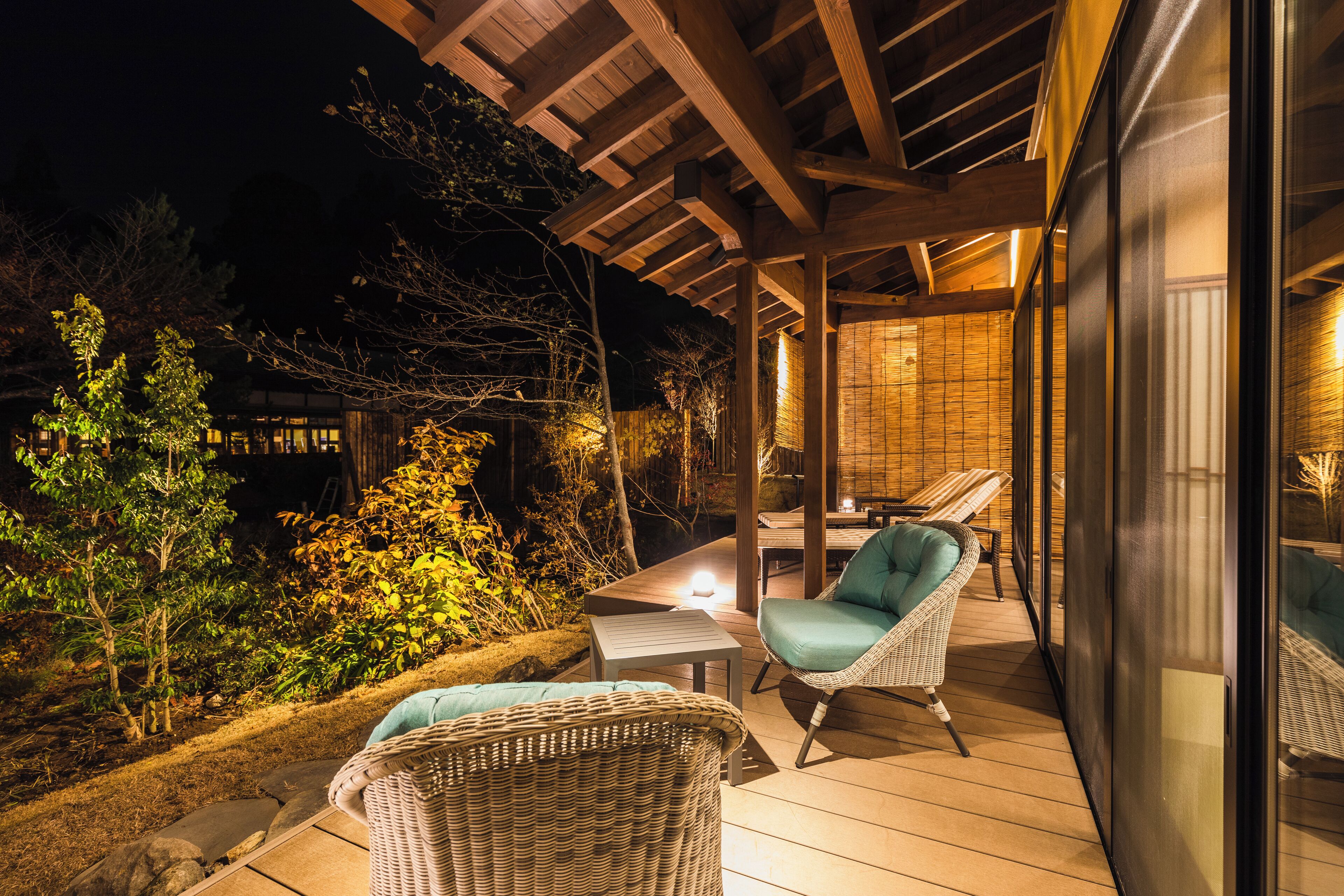 An outdoor deck with wicker furniture and a table, surrounded by greenery.