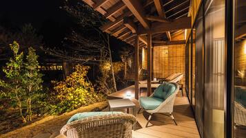 An outdoor deck with wicker furniture and a table, surrounded by greenery.