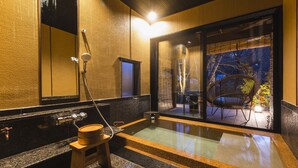 A modern bathroom with a large bathtub, a wooden stool, and a window overlooking an outdoor seating area. - tsutaonsen (Towada)