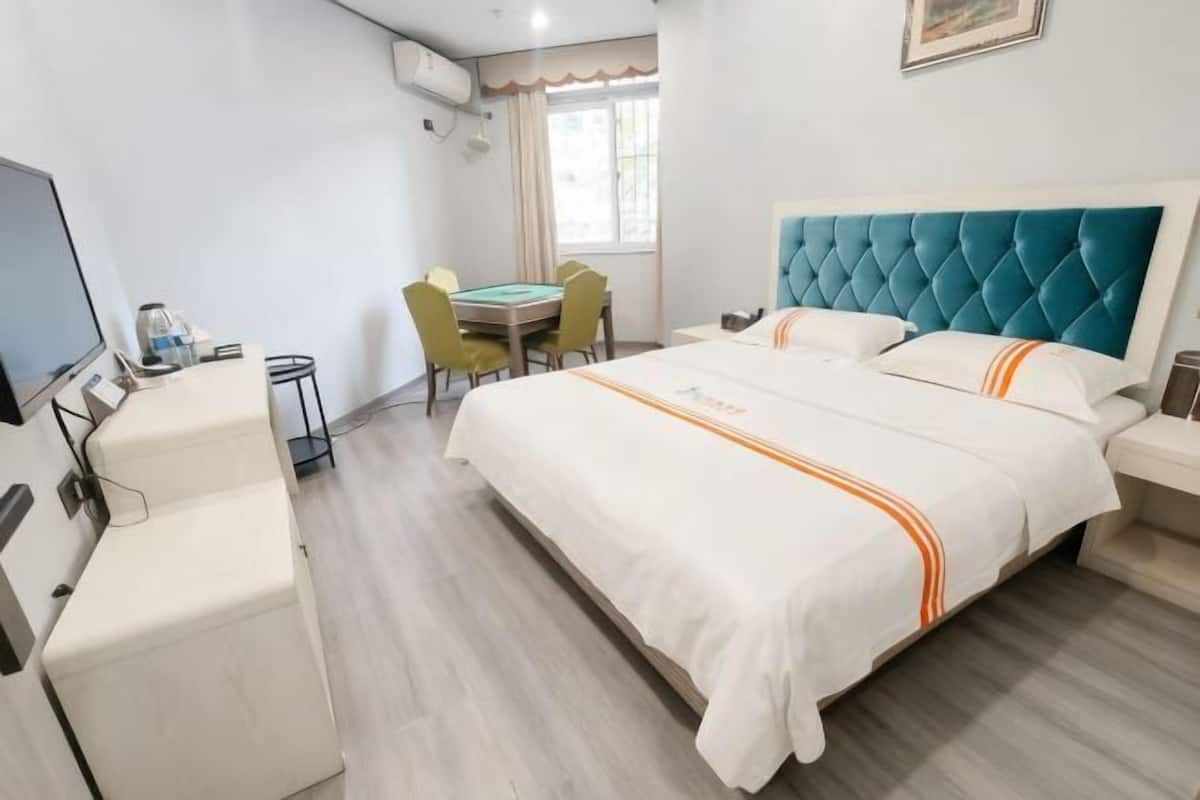 A hotel room with a bed, a desk, a chair, a table, and a television.