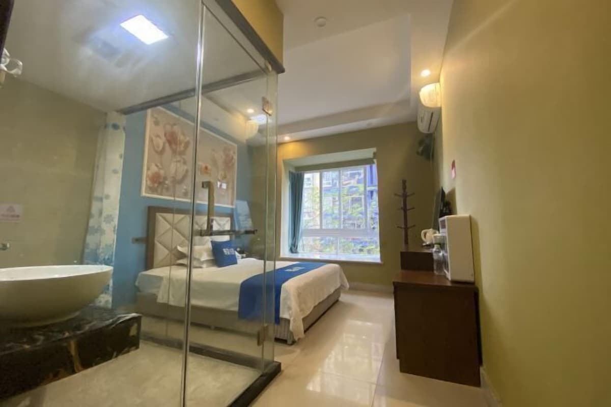 A modern bathroom with a large sink, glass shower enclosure, and a bed with a blue bedspread.