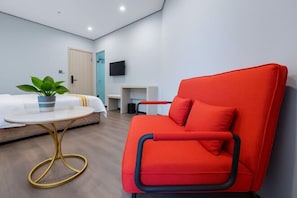 A modern hotel room with a red armchair, a bed with white bedding, a small round table with a gold base, and a potted plant on the table.