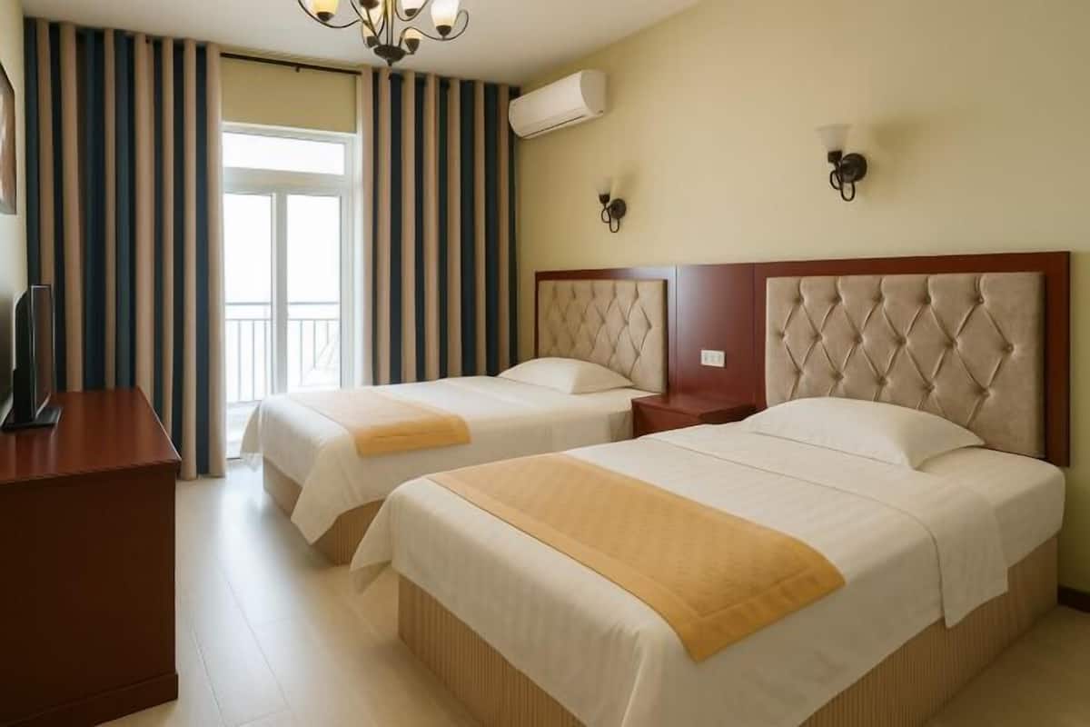 A hotel room with two beds, a wooden desk, a TV, and a balcony with striped curtains.