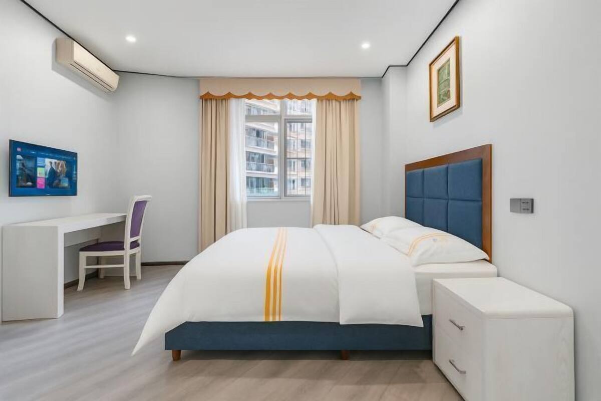 A modern hotel room with a bed, a desk, a chair, and a window with curtains.