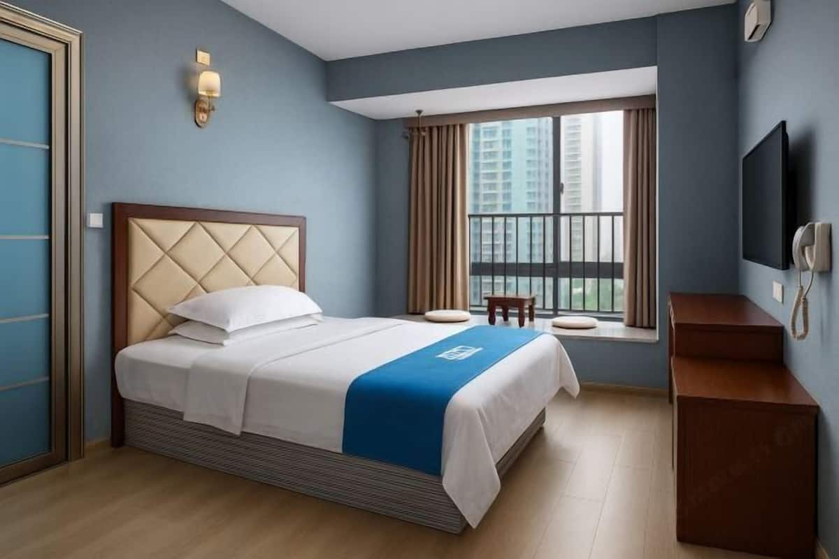 A hotel room with a bed, a window with curtains, a television, and a desk.