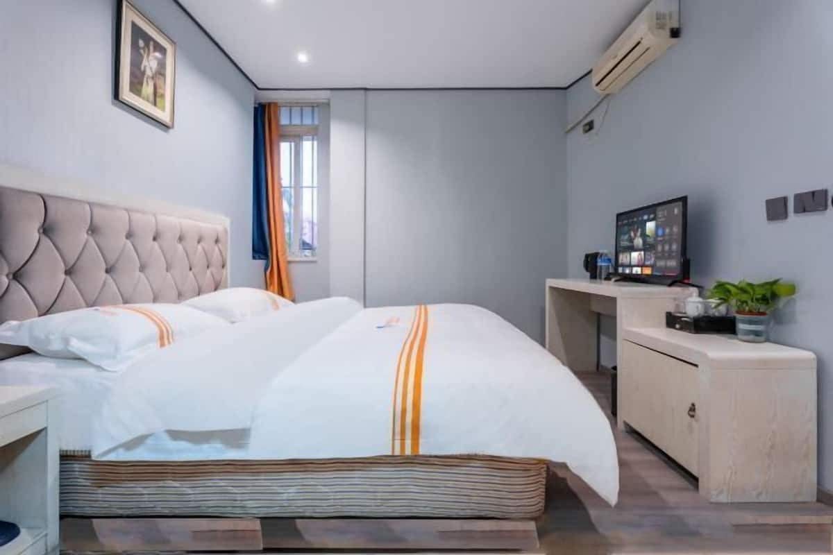 A modern hotel room with a large bed, a desk, a television, and a small cabinet.