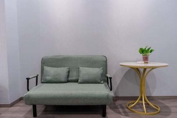 A green sofa with two cushions and a small round table with a gold base and a potted plant on top.