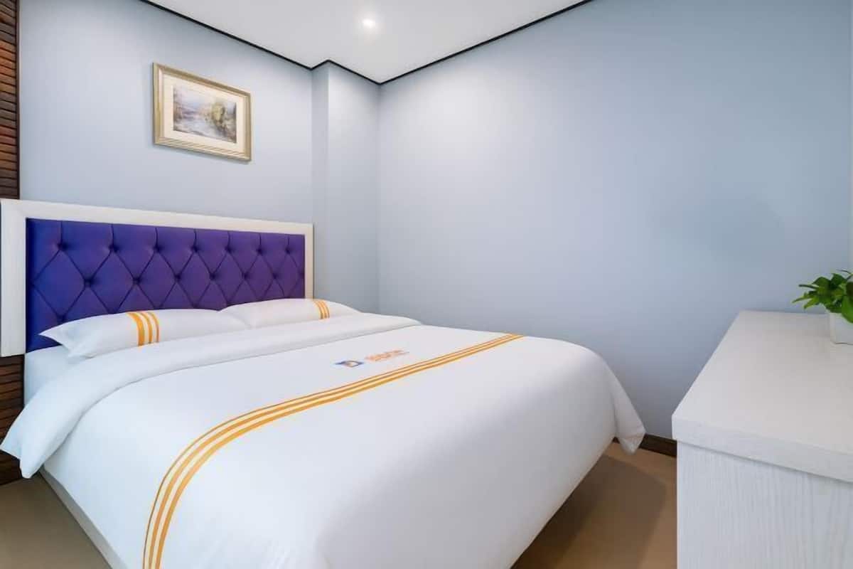 A hotel room with a large bed, a headboard, a bedside table, and a framed picture on the wall.