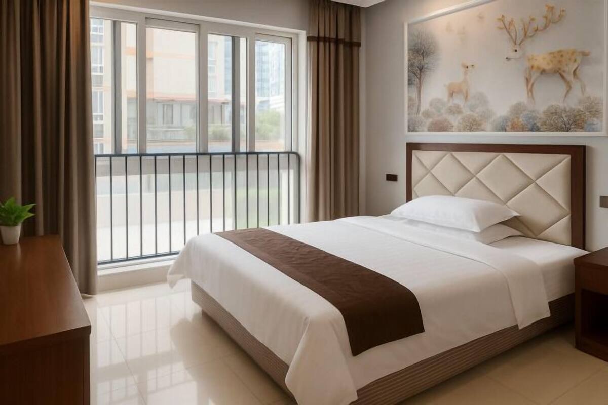 A hotel room with a large bed, a view through a balcony, and a wall-mounted deer painting.