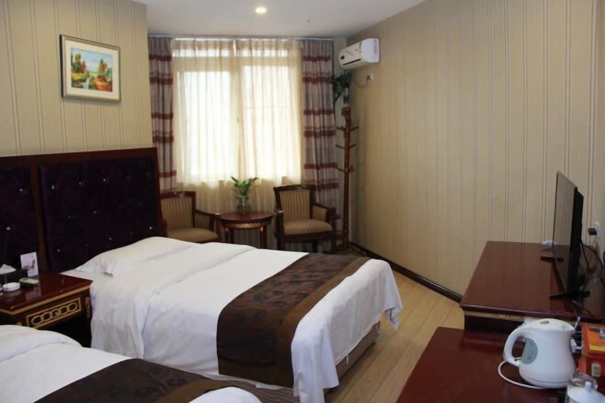 A hotel room with two beds, a desk with a kettle, a chair, and a TV.