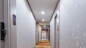 Ein Hotelgang mit Teppichboden, einer Tür rechts und einem Schild links.