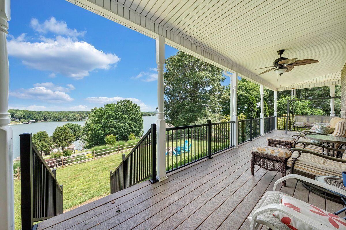 A covered porch with a view of a lake, outdoor furniture, and a ceiling fan.