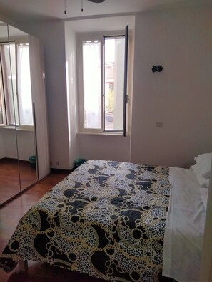 Une chambre à coucher avec un lit, une fenêtre avec des rideaux, un miroir et une porte.