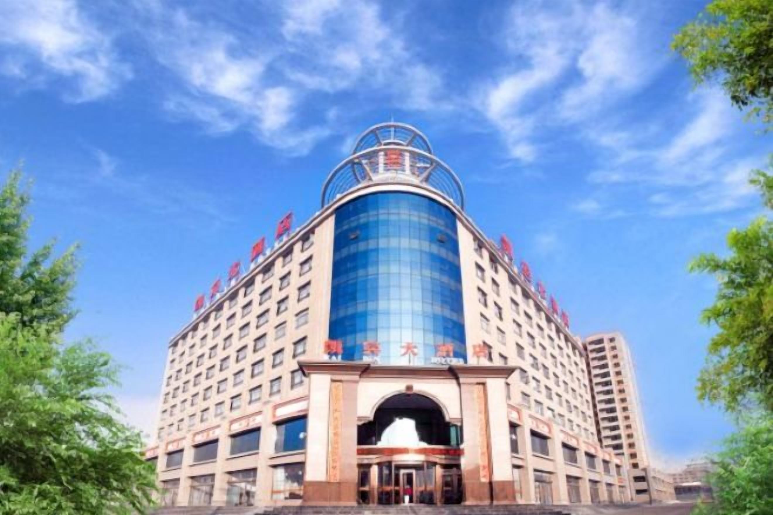 A multi-story hotel with a prominent central entrance, a large glass facade, and a rooftop structure.