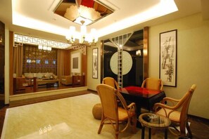 A well-lit room with a dining area featuring a table and chairs, a sofa, and a decorative wall piece. - Kai Bin Hotel (Baiyin)